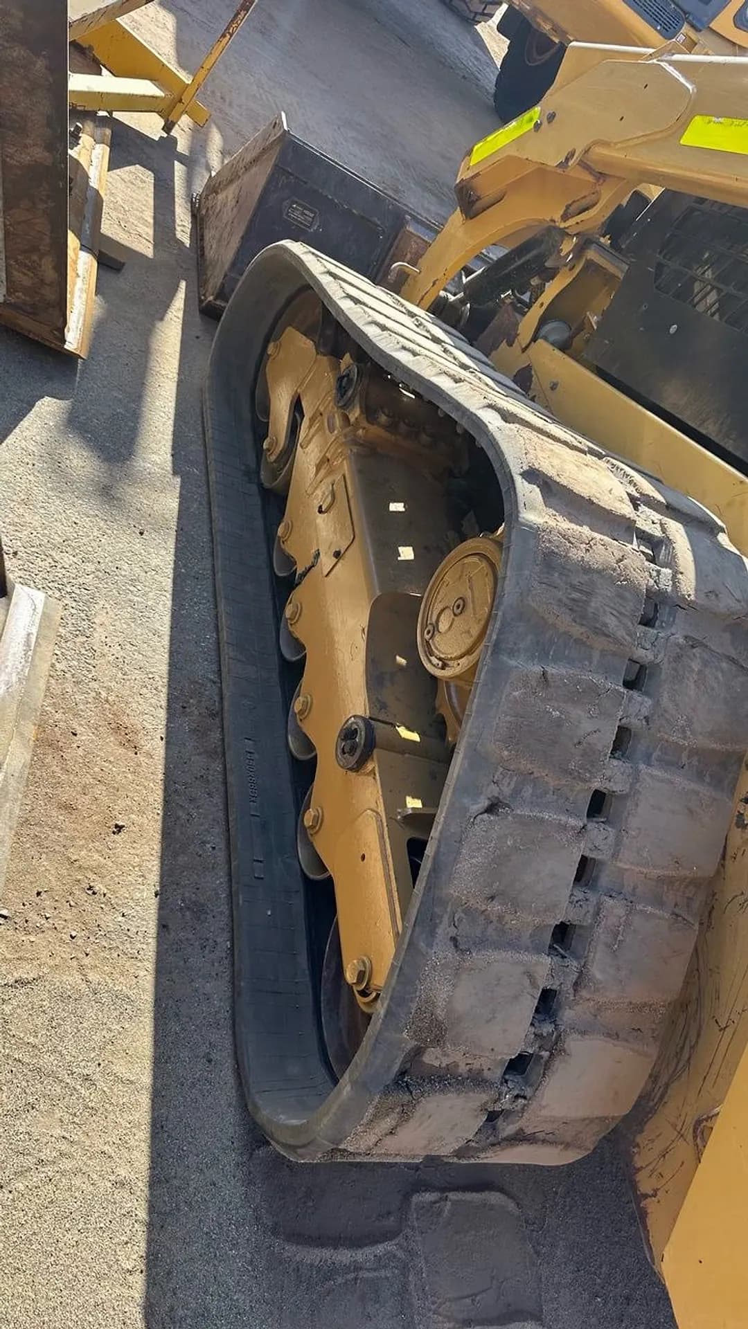 A yellow Cat skid steer with its rubber track and undercarriage exposed beside it.
